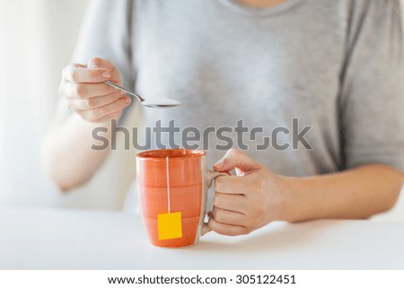 food, junk-food, drinks and unhealthy eating concept - close up of woman adding sugar to tea cup