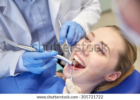 people, medicine, stomatology and health care concept - close up of dentists and assistant with mirror, drill and dental air water gun spray treating female patient teeth at dental clinic