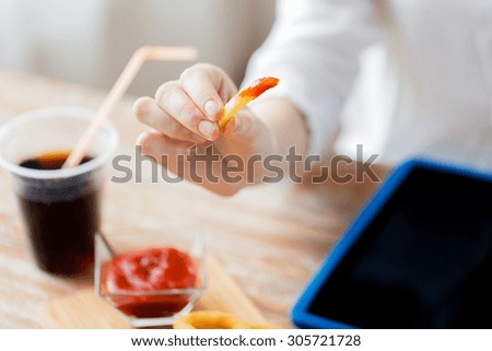 fast food, people and unhealthy eating concept - close up of woman dipping french fries into ketchup and drinking coca cola on wooden table