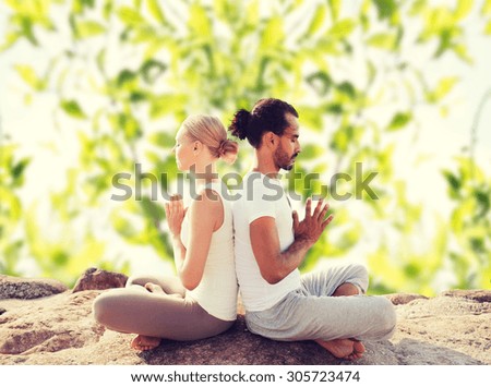 fitness, sport, meditation and lifestyle concept - smiling couple making yoga exercises sitting outdoors