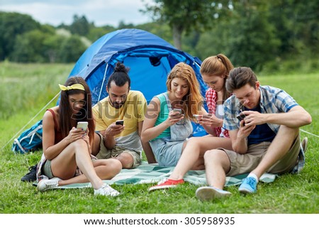 travel, tourism, hike, technology and people concept - group of friends with smartphone and tent at camping