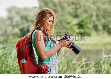 adventure, travel, tourism, hike and people concept - happy young woman with backpack and camera photographing outdoors