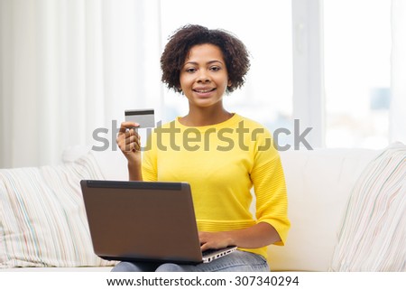 people, internet bank, online shopping, technology and e-money concept - happy african american young woman sitting on sofa with laptop computer and credit card at home