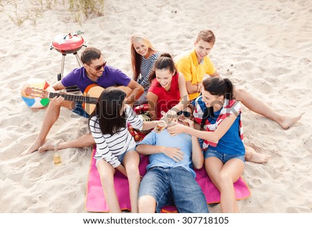 summer holidays, vacation, music, happy people concept - group of happy friends having picnic and playing guitar on beach, drinking non-alcoholic beer or soda lemonade