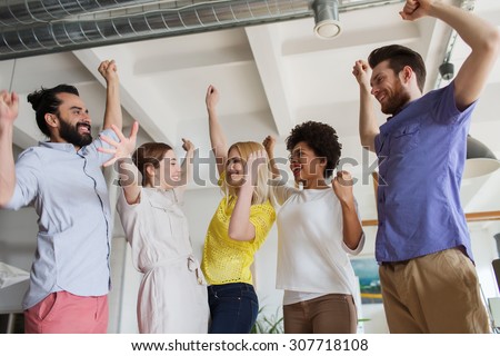 business, triumph, gesture, people and teamwork concept - happy creative team raising hands up and celebrating victory in office