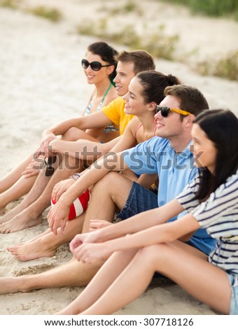 summer holidays, sport, leisure and people concept - group of happy friends sitting on beach with ball