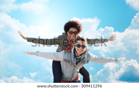 friendship, leisure, freedom and people concept - happy international teenage couple in shades having fun over blue sky and clouds background