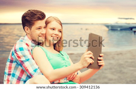 vacation, holidays, travel, technology and love concept - smiling couple with tablet pc computer taking selfie over sunset beach background