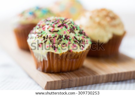 food, junk-food, culinary, baking and eating concept - close up of glazed cupcakes or muffins on wooden board
