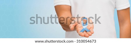 medicine, health care, gesture and people concept - close up of male hand holding blue prostate cancer awareness ribbon over blue background