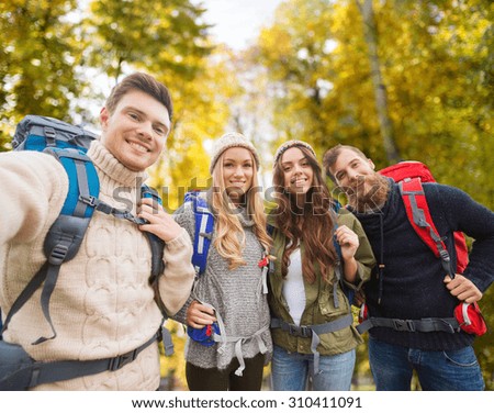 adventure, travel, tourism, hike and people concept - group of smiling friends with backpacks making selfie over natural background