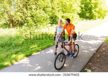 fitness, sport, summer, people and healthy lifestyle concept - happy couple with roller skates and bicycle riding and talking outdoors at park
