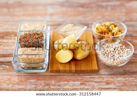 diet, cooking, culinary and carbohydrate food concept - close up of grain, pasta and beans in glass bowls with potatoes on table