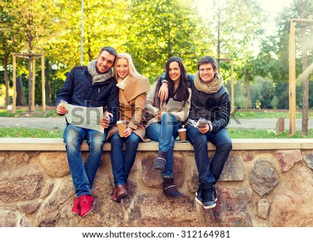 travel, vacation, people, tourism and friendship concept - group of smiling friends sitting with tablet pc computer map and hot drinks in park