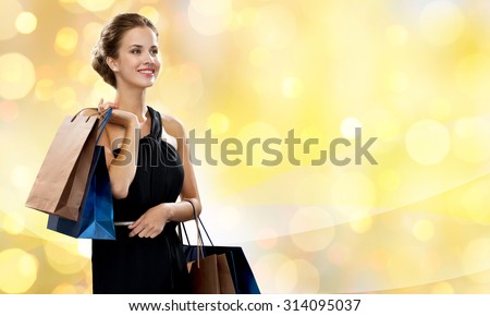 luxury, advertisement, holydays and sale concept - smiling woman with shopping bags over yellow lights background