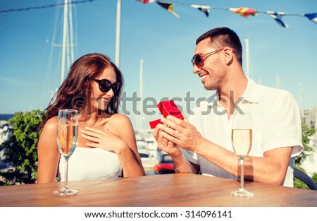 love, dating, people and holidays concept - smiling couple wearing sunglasses with champagne and red gift box looking to each other at cafe
