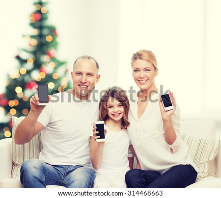 family, holidays, technology and people - smiling mother, father and little girl with smartphones over living room and christmas tree background