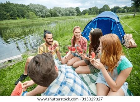 travel, tourism, hike, picnic and people concept - group of happy friends with tent eating watermelon at camping