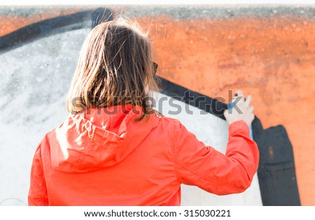 people, art, creativity and youth culture concept - young woman or teenage girl drawing graffiti with spray paint on street wall from back