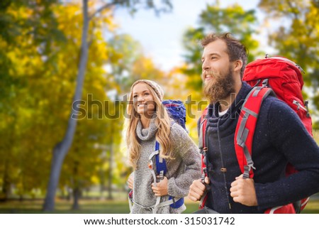 adventure, travel, tourism, hike and people concept - smiling couple walking with backpacks over autumn forest background