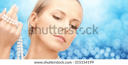 beauty, luxury, people, holidays and jewelry concept - beautiful woman with sea pearls beads in hand over blue lights background