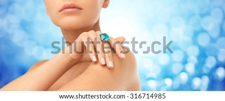 people, jewelry, luxury and glamour concept - close up of woman wearing ring with precious gem over blue lights background