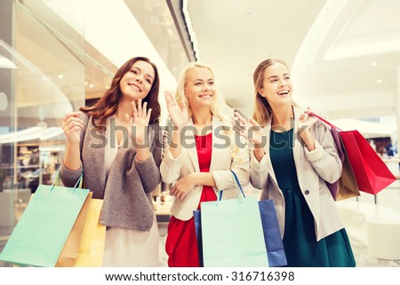 sale, consumerism and people concept - happy young women with shopping bags waving hands in mall