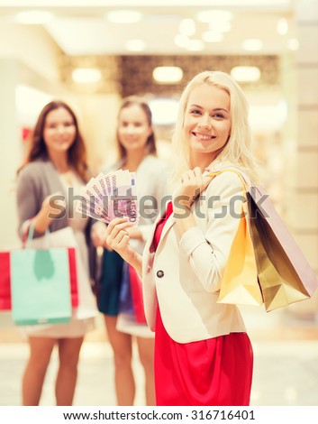 sale, consumerism and people concept - happy young women with shopping bags and euro cash money in mall