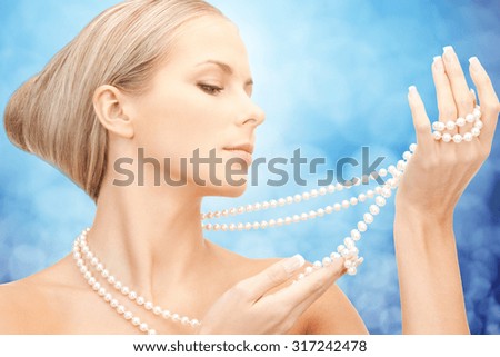 beauty, luxury, people, holidays and jewelry concept - beautiful woman with sea pearl necklace or beads in hands over blue lights background