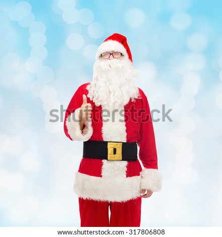 christmas, holidays, gesture and people concept- man in costume of santa claus showing thumbs up over blue lights background