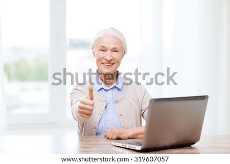 technology, age and people concept - happy senior woman with laptop computer at home showing thumbs up gesture
