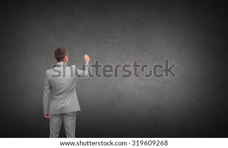 business, people, advertisement , information and office concept - businessman writing or drawing something imaginary from back over dark gray concrete wall background
