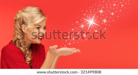 people, holidays, christmas, magic and winter concept - lovely woman in red clothes sending stars from on palms of her hands over red background
