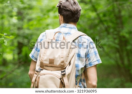 adventure, travel, tourism, hike and people concept - young man with backpack hiking in woods from back
