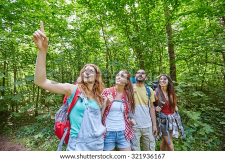 adventure, travel, tourism, hike and people concept - group of smiling friends with backpacks pointing finger up in woods