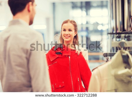 sale, shopping, consumerism and people concept - happy young couple choosing clothes at clothing store in mall