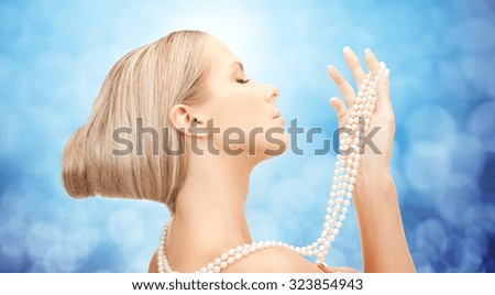 beauty, luxury, people, holidays and jewelry concept - beautiful woman with sea pearl necklace or beads in hand over blue lights background
