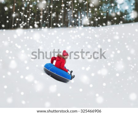 winter, leisure, sport, and people concept - happy teenage girl or woman sliding down on snow tube