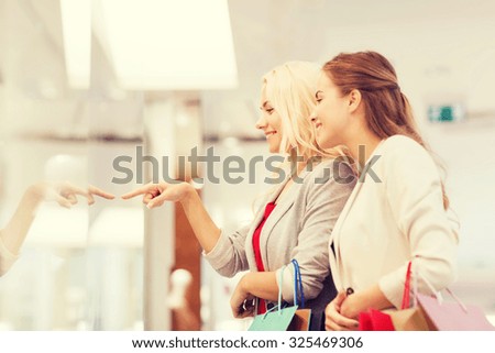 sale, consumerism and people concept - happy young women with shopping bags pointing finger in mall