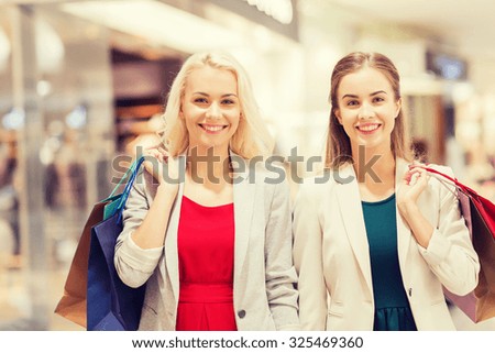 sale, consumerism and people concept - happy young women with shopping bags in mall