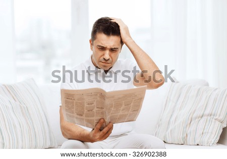 leisure, information, people and mass media concept - sad man reading newspaper at home