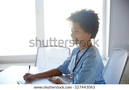 health care, profession, people and medicine concept - happy female doctor or nurse with clipboard and pen writing at hospital