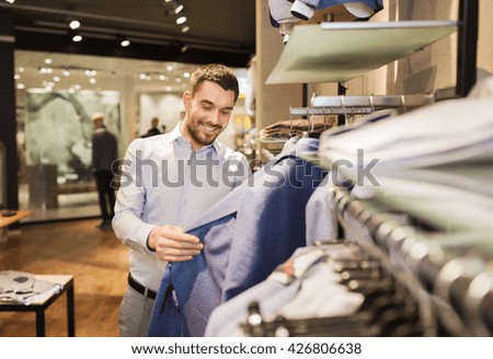 sale, shopping, fashion, style and people concept - happy young man in shirt choosing jacket in mall or clothing store 商業照片 © 