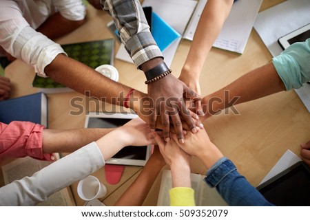 education, school, teamwork and people concept - close up of international students with hands on top of each other sitting at table