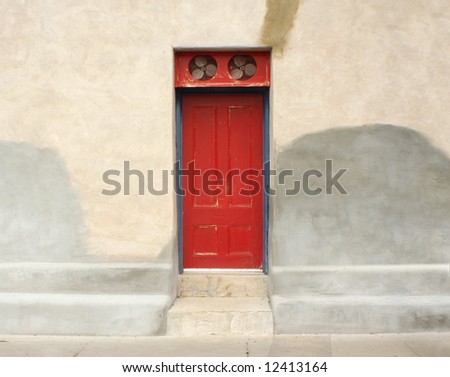 Antique unique red door with fans above it & adobe wall