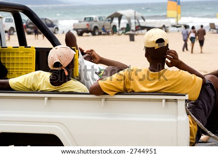 Men resting on back of truck at the beach.