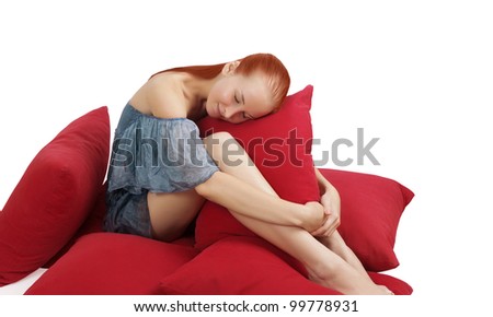 Young woman sitting with a bunch of red pillows, resting her head on one, isolated on white background.