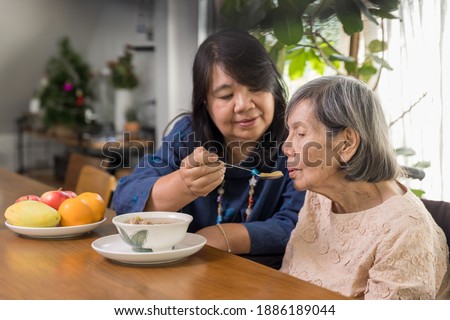 Daughter feeding elderly mother with soup.