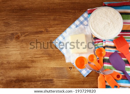 top view of baking ingredients - dough, eggs, flour, butter, and kitchen utensils over wood board.
