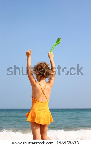 back view of little girl standing at the beach with hands waved